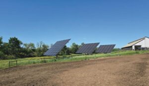 Three dual-axis solar trackers beside a plowed field on a Chambersburg farm