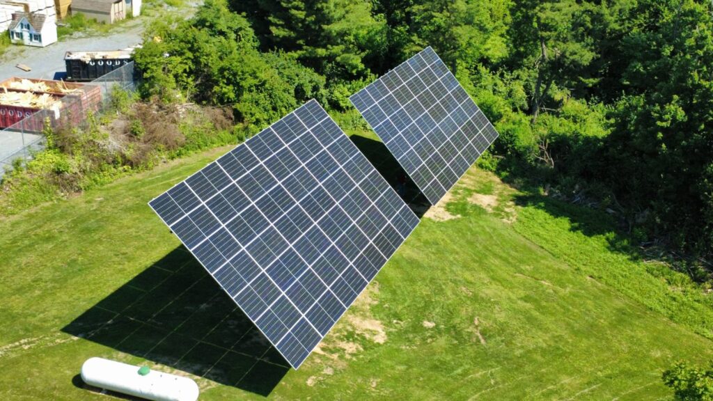 Two pole-mounted dual-axis solar trackers tilted toward the sun on a lawn