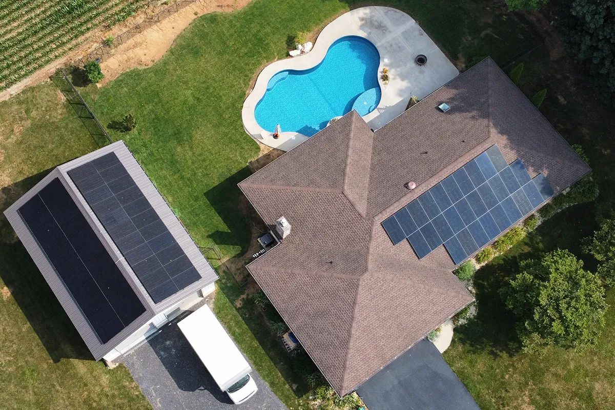 Aerial view of a home and garage with rooftop solar panels beside a pool